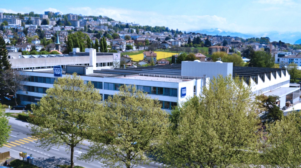 WORKPRO industrial complex in Switzerland with blue window bands, sawtooth roofs and trees along the street WORKPRO industrial complex in Switzerland with blue window bands, sawtooth roofs and trees along the street